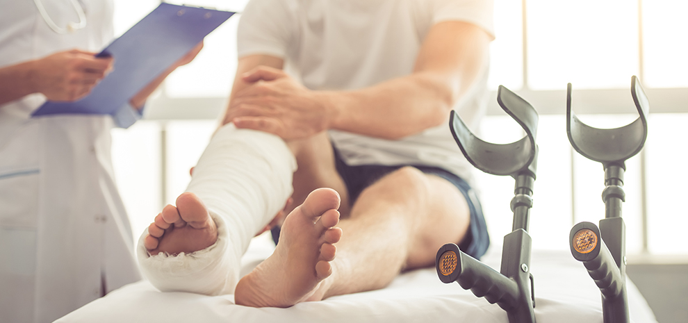 Cropped image of female medical doctor listening to patient with broken leg and making notes while working in her office